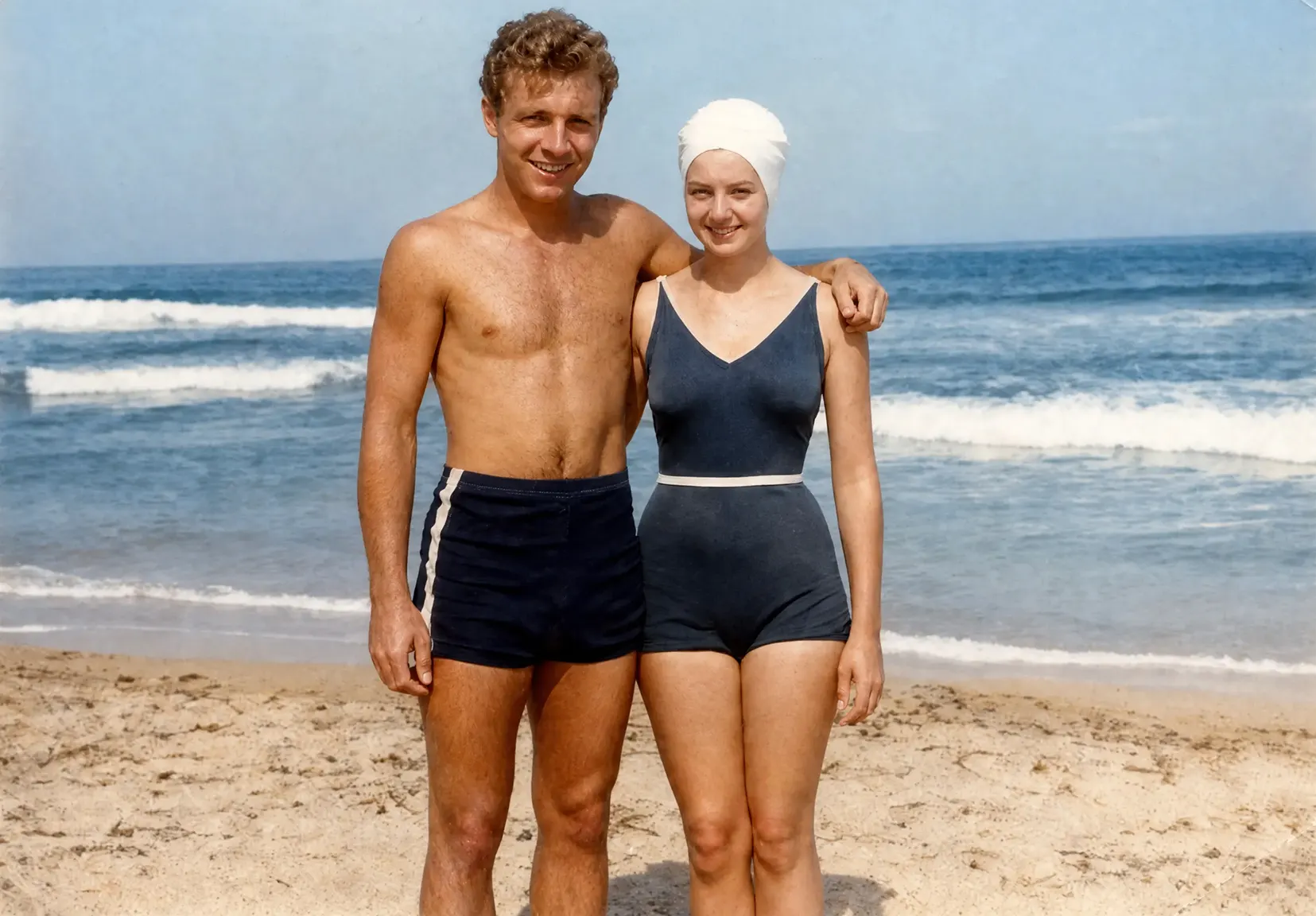 Restored beach photo: a young couple in mid-century swimsuits arm in arm at the shoreline
